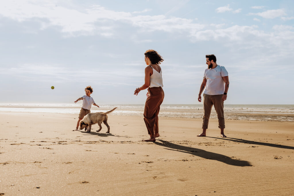 Séance photo à Oye-Plage, prise à la plage. Montrant une famille jouant sur le sable à lancer la balle à leur chien